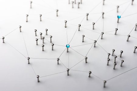 Network of various metallic pins stuck into a white board and connected via thin lines of wire.