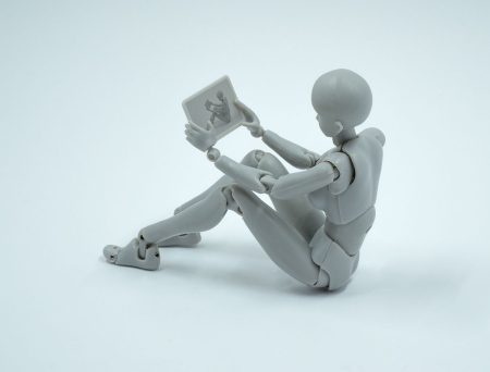 Robot figurine sitting on the ground with a tablet in its hands, and its display shows this very scene (like an endless reflection).